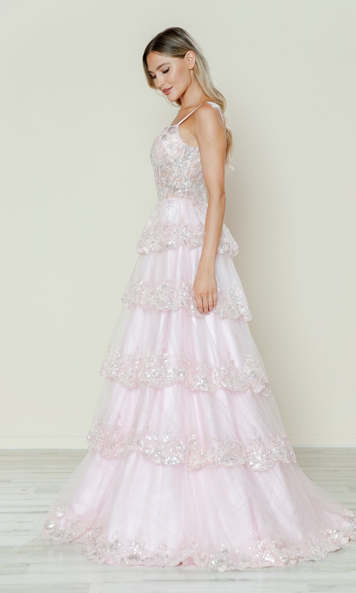 A woman stands in profile wearing the Long Glitter-Lace Tiered Prom Dress (Poly USA 9548), a floor-length pale pink gown with sequin embellishments, evoking classic Southern style against a light background.
